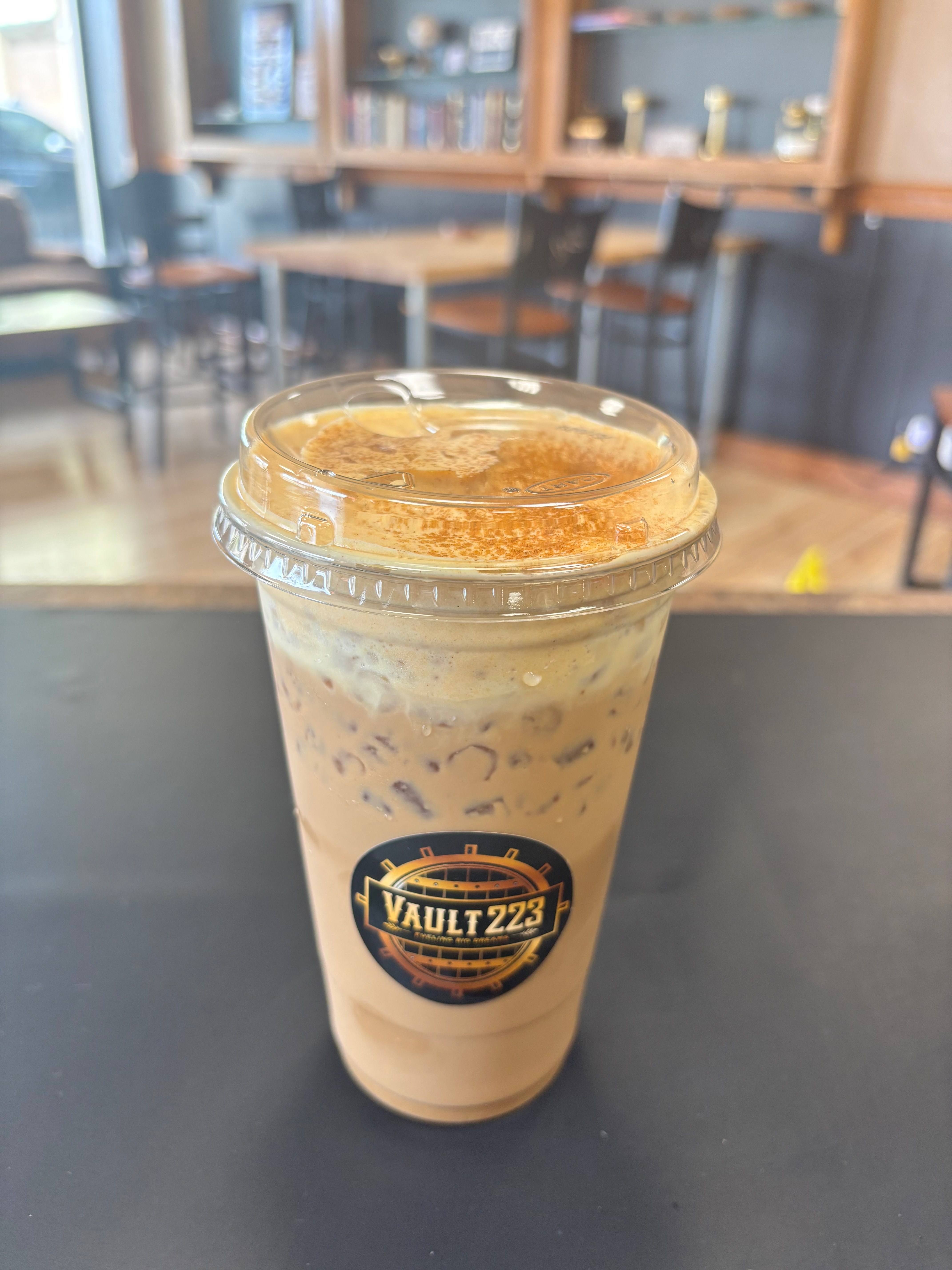 A branded iced drink on the counter with Vault 223 café seating in the background